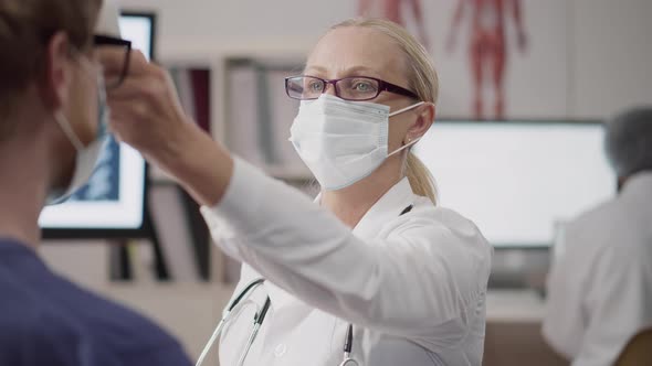 Doctor in Safety Mask Scan Patient Temperature with Infrared Thermometer