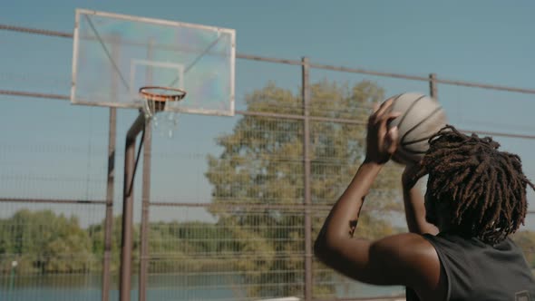 Man Trains Throwing Basketball Ball in Basket on a Street Court on a Sunny Day