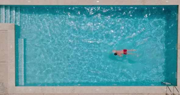 View From the Top As a Man in Red Shorts Swims in the Pool