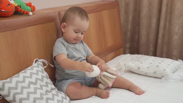 Baby girl 12-17 months old playing with a knitted toy rabbit sitting on the parent's bed bedroom