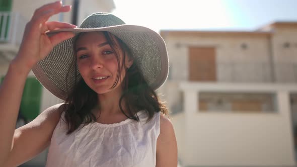 Portrait of Smiling Young Woman in Sunrays Looking at Camera at Background of Ancient Town on Cyprus