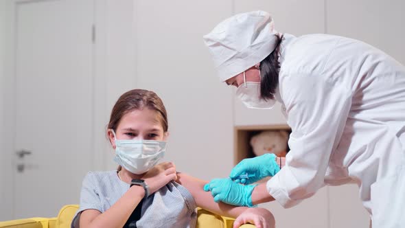 A Nurse in Protective Gloves and a Protective Mask Gives an Injection to a Young Girl