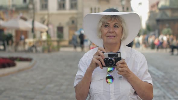 Senior Female Tourist Exploring Town and Makes a Photo with Retro Photo Camera