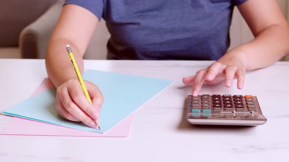 Woman is using a calculator to calculate her monthly expenses and write down her monthly accounting