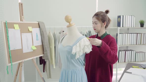 Asian female designer working measuring dress on a mannequin clothing design at the studio.