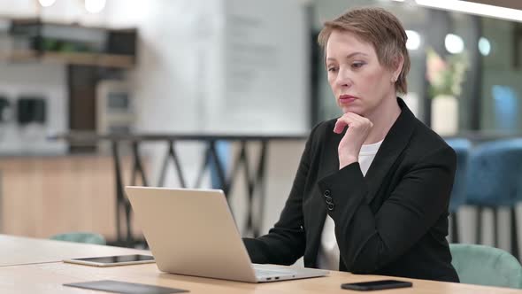 Old Businesswoman Thinking and Working on Laptop in Office
