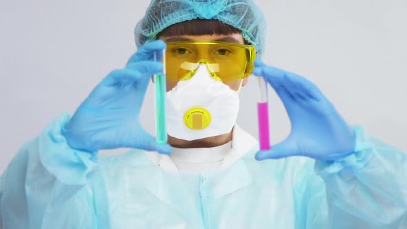 Close-up of Scientist in Protection Mask and Glasses Holding Two Test Tubes with Samples of Pink 