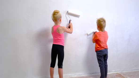 Blonde Boy and Girl Making Repairs at Home Brother and Sister Painting Paint Roller Wall White Paint