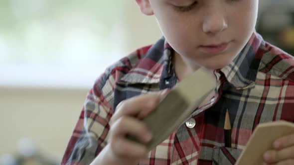 Young boy in a wood shop sanding a piece of wood.