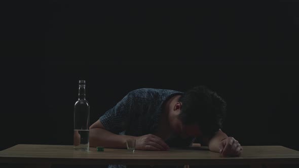 Drunk Asian Man Pouring Vodka In A Shot Glass Before Drinking And Sleeping In Black Background