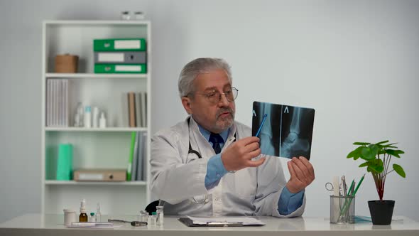 Aged Male Doctor in White Medical Coat Advises Patient By Pointing Out Disease on Picture and