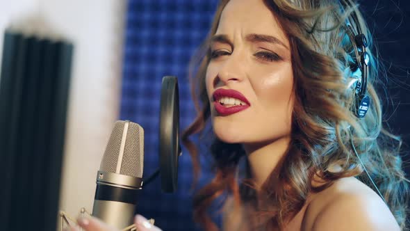 Young woman recording a song in a professional studio. The girl sings into the microphone.