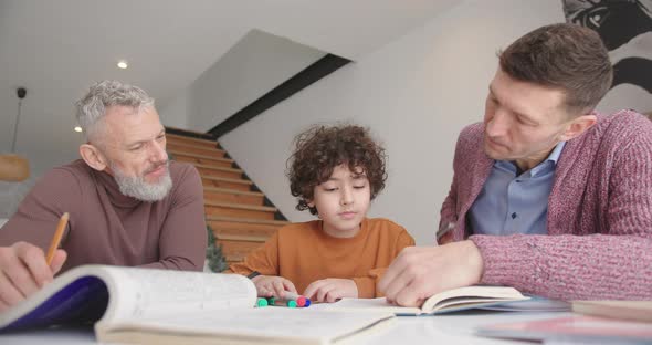 Gay Parents Help Little Son with Homework Sitting at Desk