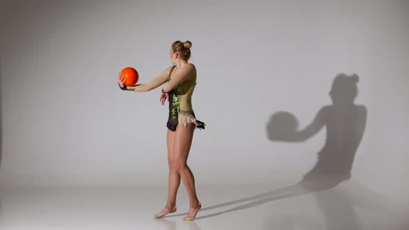 Gymnast Doing Acrobatic Moves with the Ball and Get on One Leg. White Background