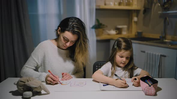 A Mother and a Small Daughter Draw Drawings on Paper in the Kitchen with Markers