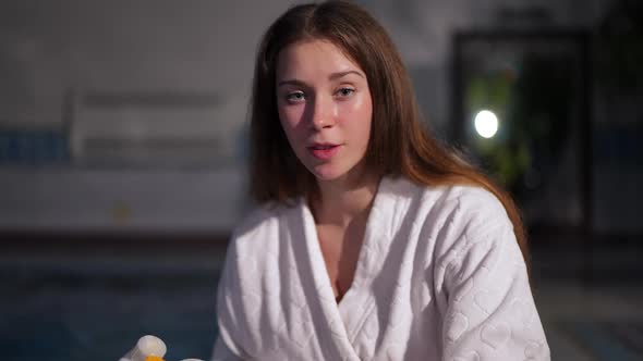 Young Charming Woman Smiling Looking at Camera Sitting at Pool with Moisturizer