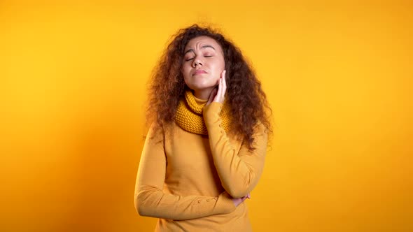 Young Beautiful Upset Woman with Curly Hair on Yellow Studio Portrait