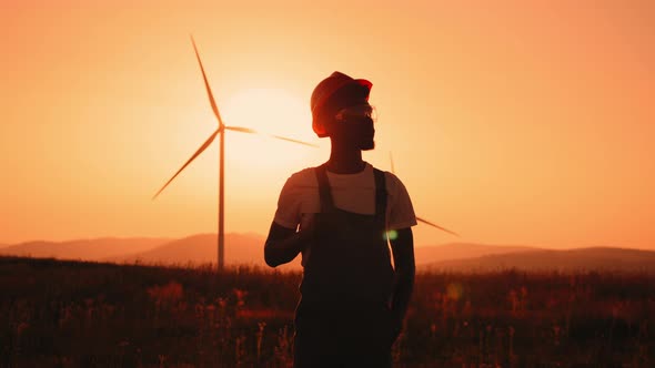 Silhouette African Man Standing on Field with Huge Windmills During Summer