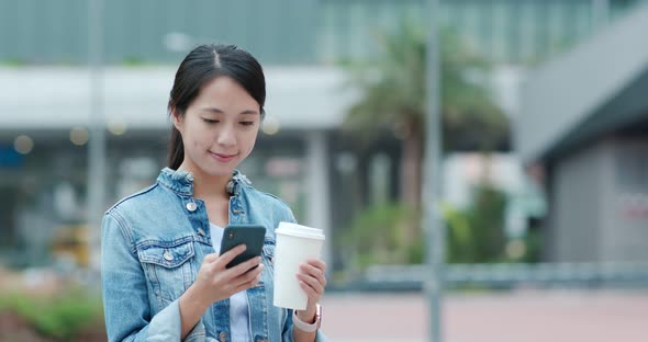 Woman use of mobile phone and holding coffee cup