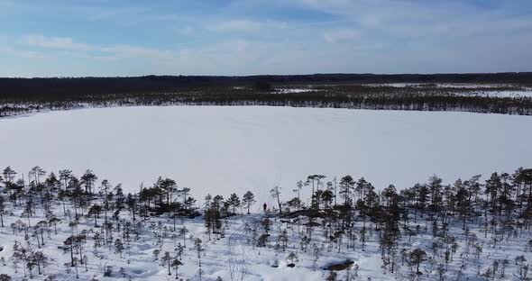 A Woman is Walking Out of the Forest to the Frozen Lake