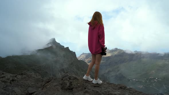 Beautiful Traveler Woman in a Pink Sweater Stands on the Edge of a Cliff and Enjoys the View of the
