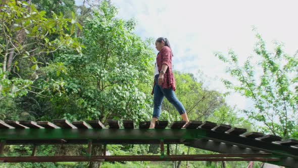 A beautiful Asian woman walking on a wooden bridge across a stream in a mountain forest.