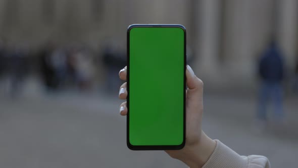 Woman Holding and Touching Phone with Green Screen Vertically in the Street