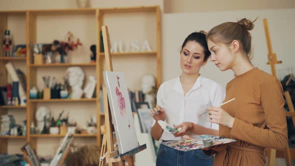 Experienced Painting Teacher Is Talking To Her Female Student Standing Near Picture on Easel and