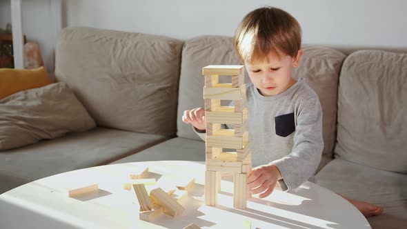 Child Crash a Tower From Wooden Blocks Sitting on the Sofa at Home