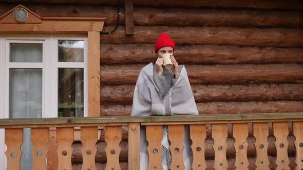 Woman in a Knitted Red Hat and Scarf Drinks Hot Tea Standing