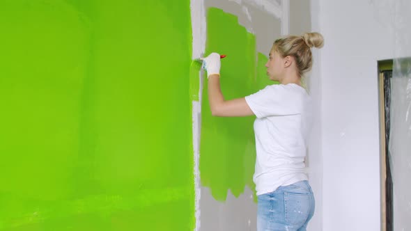 A Beautiful Young Woman in Jeans and a White Tshirt is Painting the Wall Green