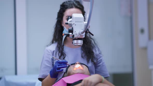 Front View Patient in Dentist Chair with Doctor Using Dental Endodontic Binocular Microscope and