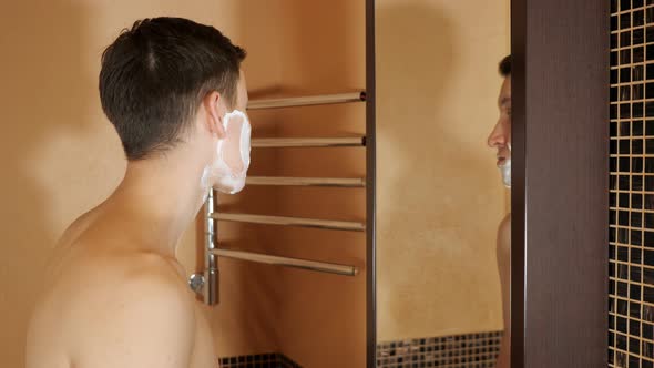 Handsome Man Shaves in Front of a Mirror