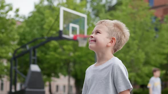 Portrait of Cute Blonde Preschooler Boy at Basketball Playground Looking at Camera