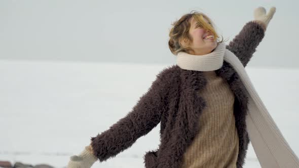 Excited young woman playing in snowy winter woods while rejoicing with her arms open wide