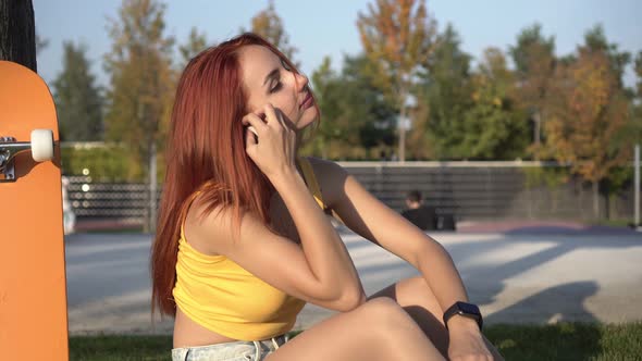 Young Beautiful Woman Teenager in the Park Listens to Music Using Wireless Headphones