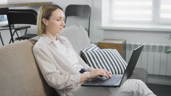 Pleasant Young Woman in Her Apartment Using a Modern Laptop for Work Online Shopping and