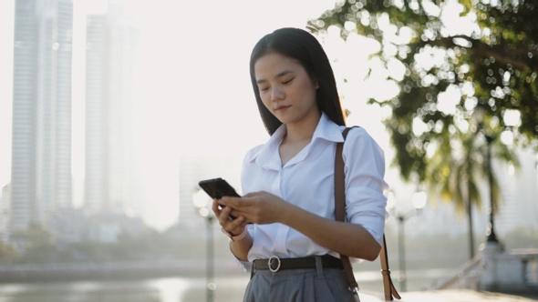 An Asian businesswoman in a white shirt is using a smartphone to send a message or email for work.