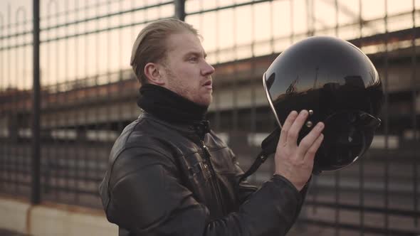 Young Attractive Man Motorcyclist with His Helmet and Custom Motorcycle on Street