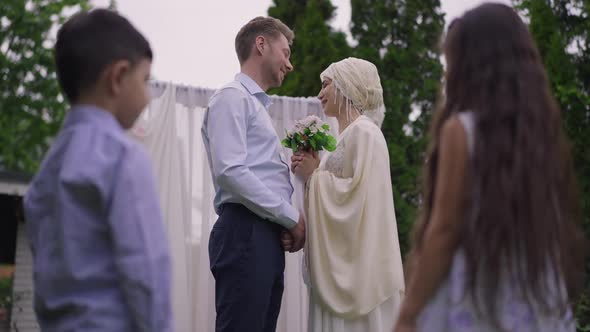Side View of Happy Middle Eastern Woman and Caucasian Man Talking on Wedding Day with Blurred