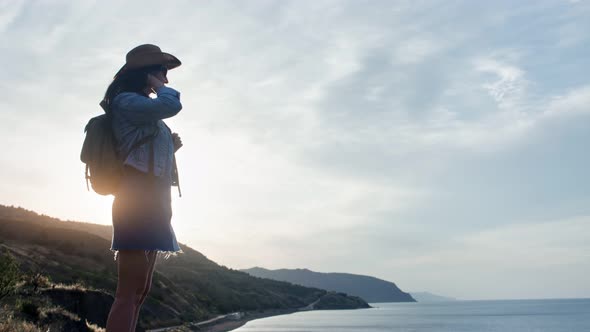 Enthusiastic Young Travel Woman with Backpack Admiring Seascape at Sunset From Top of Mountain