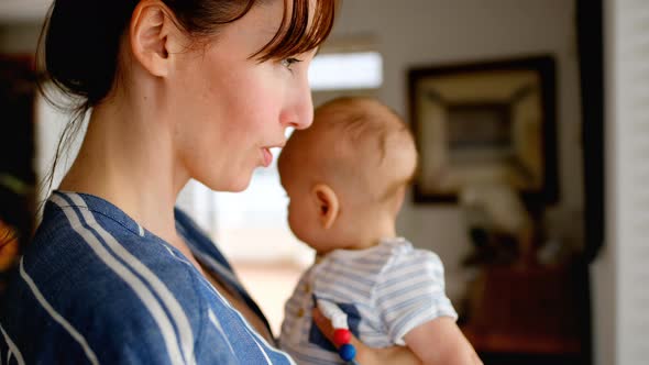 Young mom standing near window while holding baby 4k