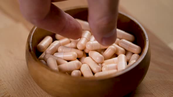 A hand takes a capsule of vitamin B complex from a full wooden eco bowl close-up in slow motion