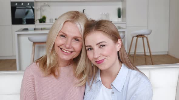 Happy Two Women Adult Daughter Hugging Her Mother Smiling and Looking at Camera While Sitting at