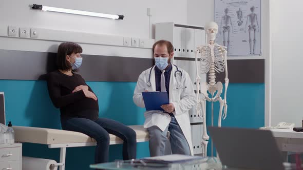 Physician Taking Notes on Papers at Checkup Visit with Pregnant Patient