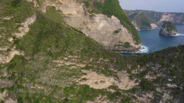 Aerial pull back of man standing on steep ridge overlooking kelingking beach