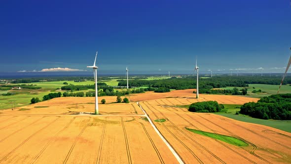 Aerial view of wind turbines and golden field near highway.