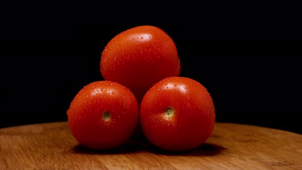 Ripe red tomatoes with droplets of condensation lie on a board against a black background