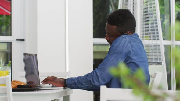 African american businessman using laptop and talking on smartphone in cafe