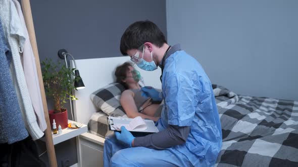 Male Medical Worker in Blue Uniform and Woman Patient with an Oxygen Mask Lie on Bed at Home